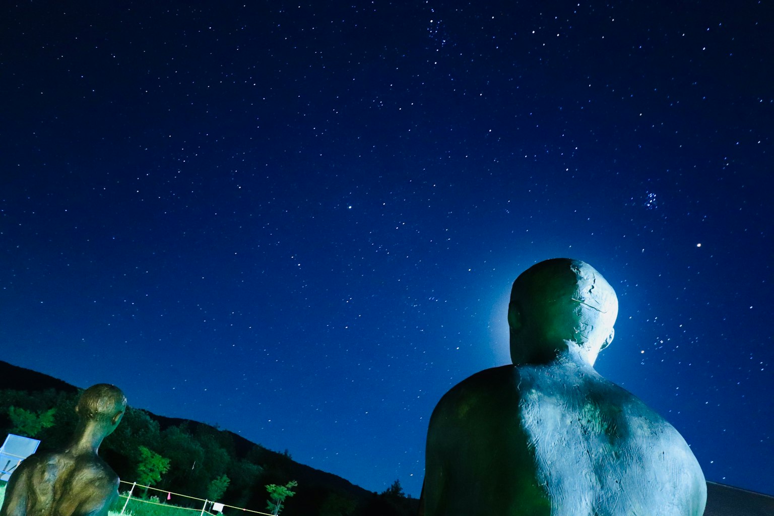 Human sculptures gazing at a starry night sky