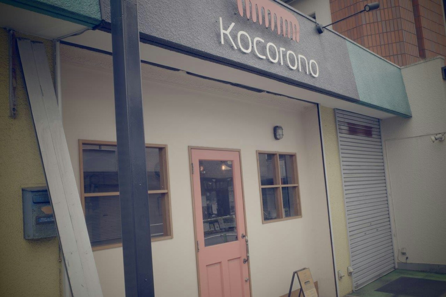 Extérieur d'une boutique avec le panneau Kocorono mettant en avant une porte rose et des fenêtres