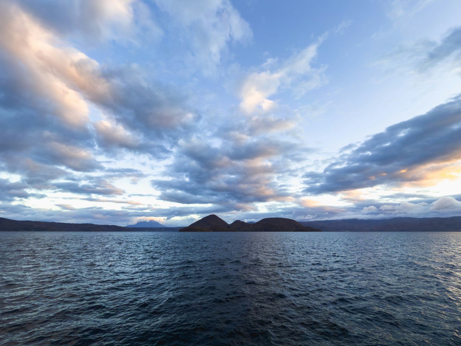 Vista panoramica di acqua blu e cielo ampio con nuvole luce del tramonto che illumina le montagne