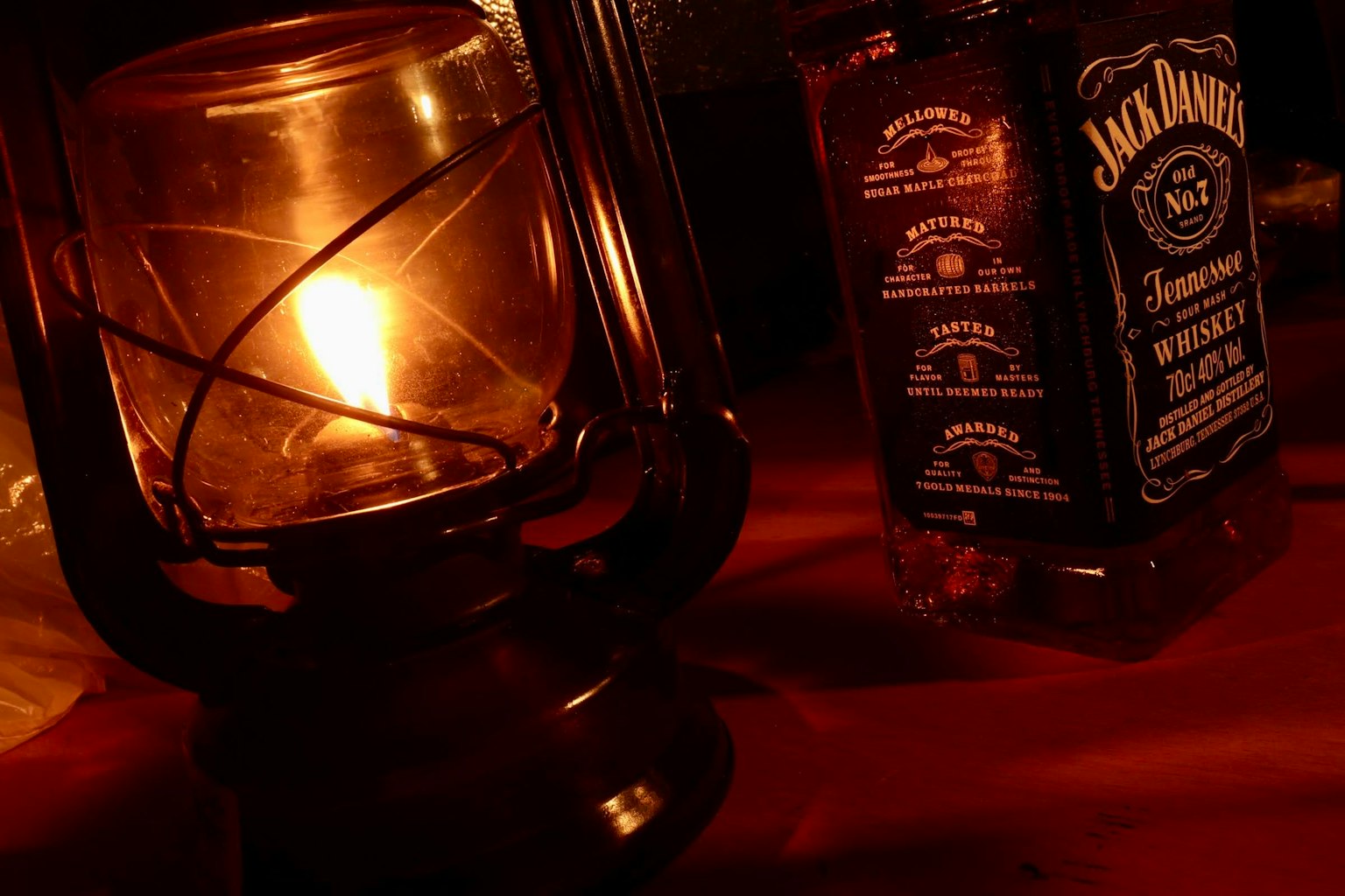 Una linterna que emite una luz cálida junto a una botella de whisky Jack Daniel's en un ambiente acogedor