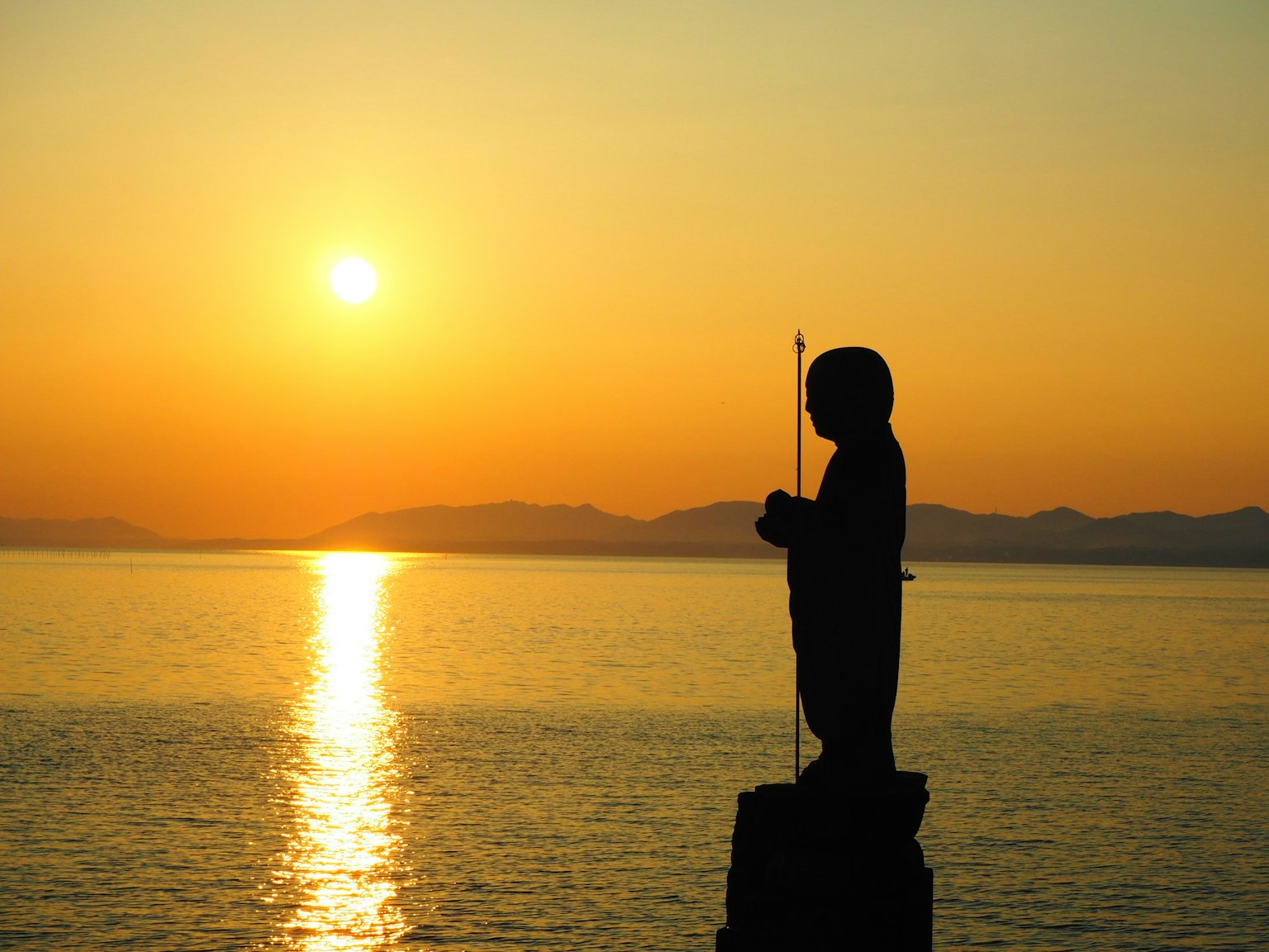 Silhouette of a child statue standing by the sea at sunset