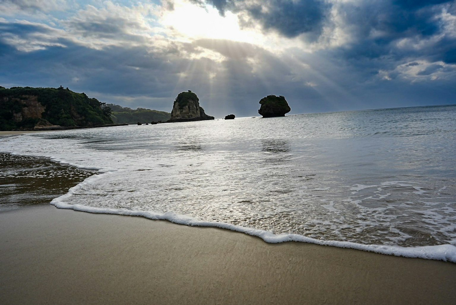 ฉากชายหาดที่มีคลื่นและหิน แสงแดดส่องผ่านเมฆ