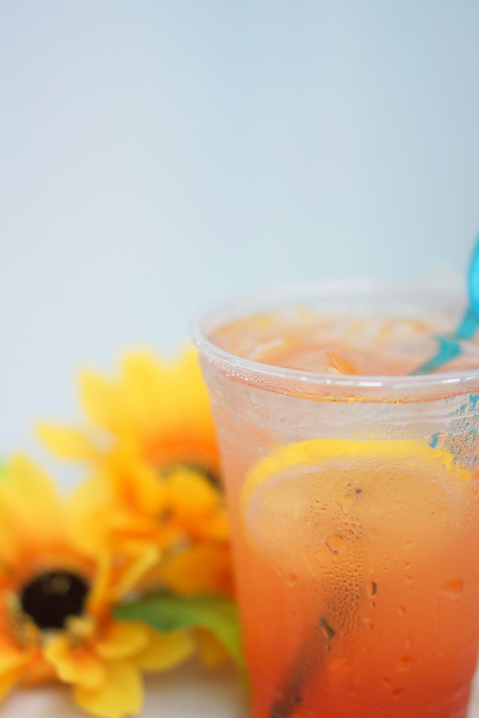 Transparent cup with orange drink and yellow sunflower flowers