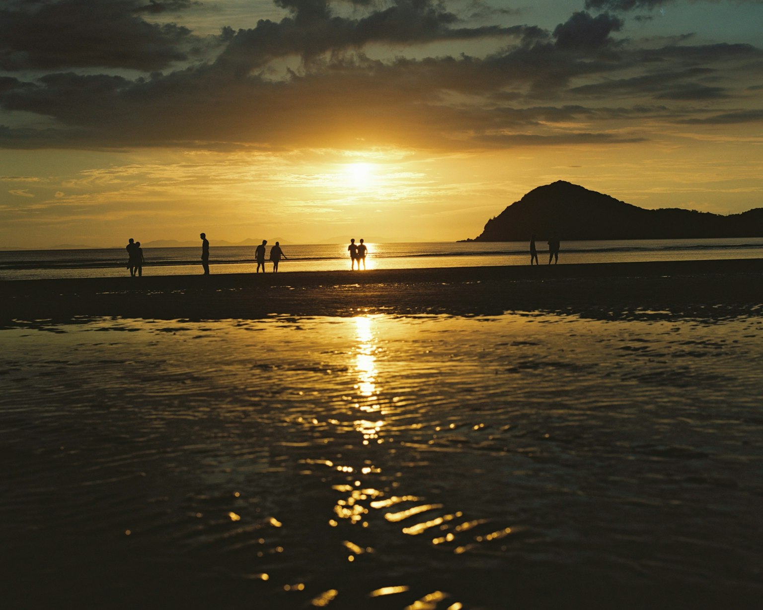Scenic beach at sunset with reflections on water and silhouettes of people