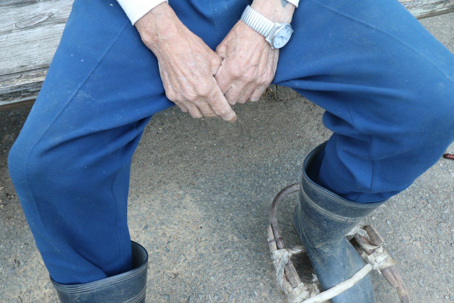 Close-up of a man's hands resting on his blue pants while wearing rubber boots