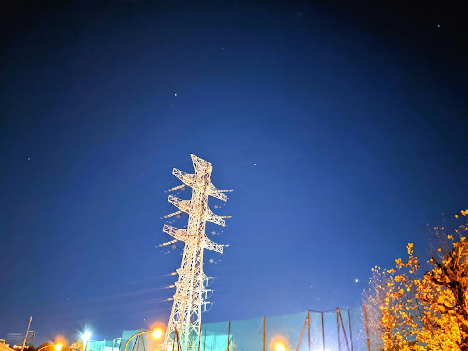 Ein hoher Strommast vor einem Nachthimmel mit umliegenden Lichtern