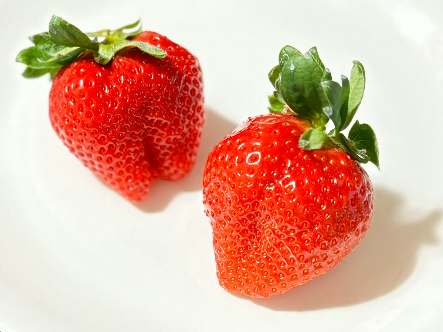 Two fresh strawberries placed on a white plate