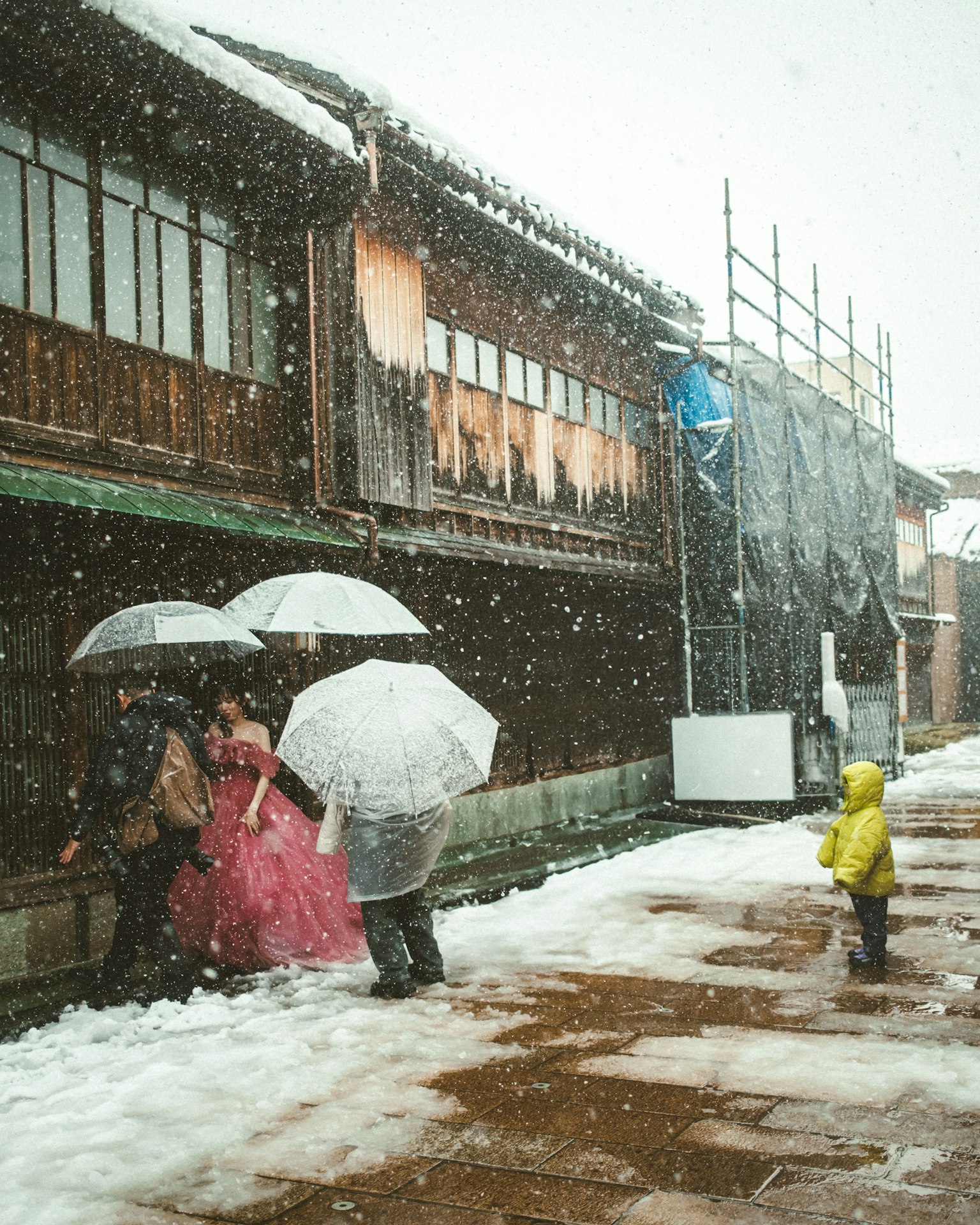 在雪中打着伞的人们走在传统建筑旁边
