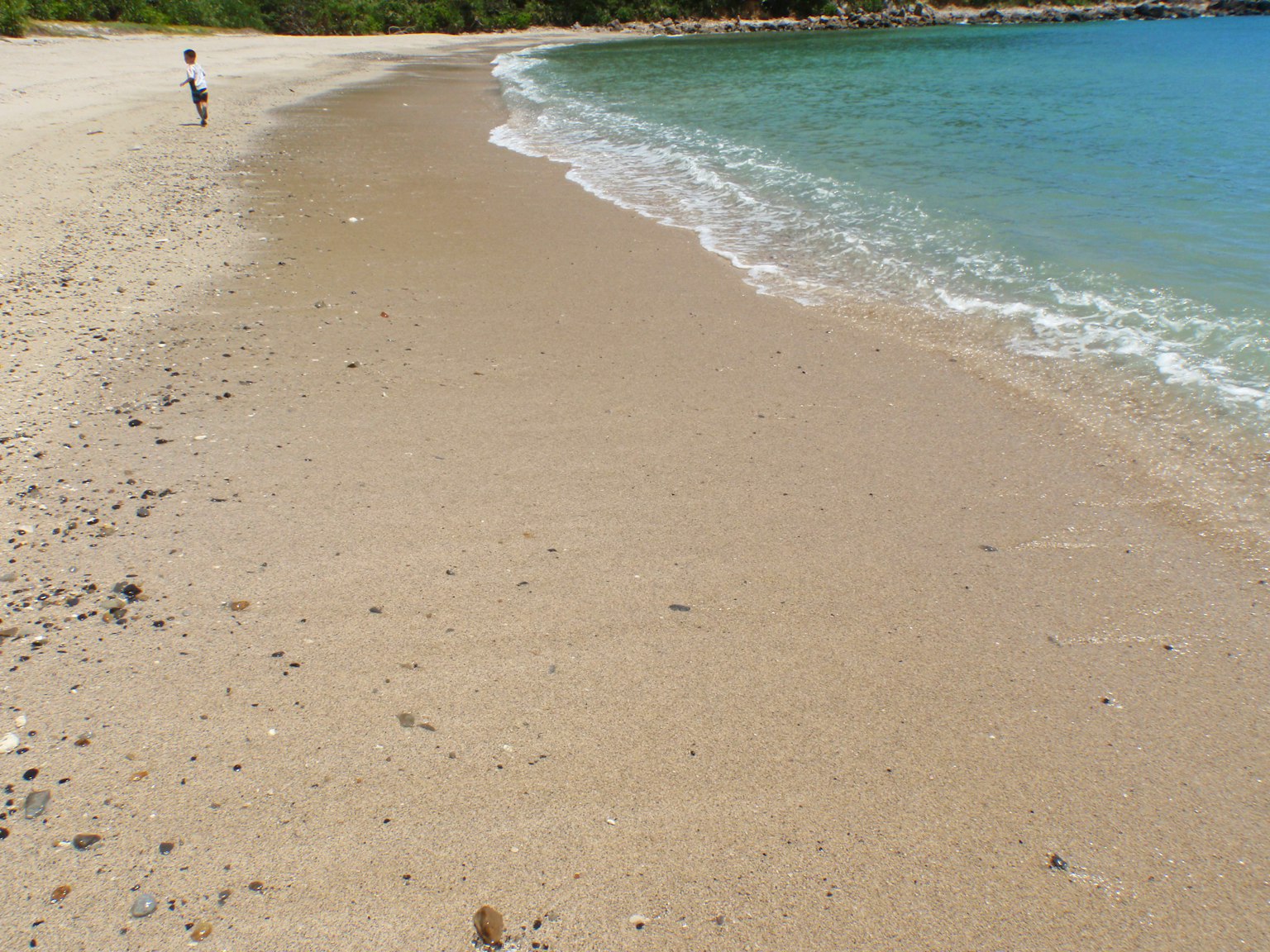 Scène de plage montrant le rivage sablonneux et des vagues douces avec une personne marchant