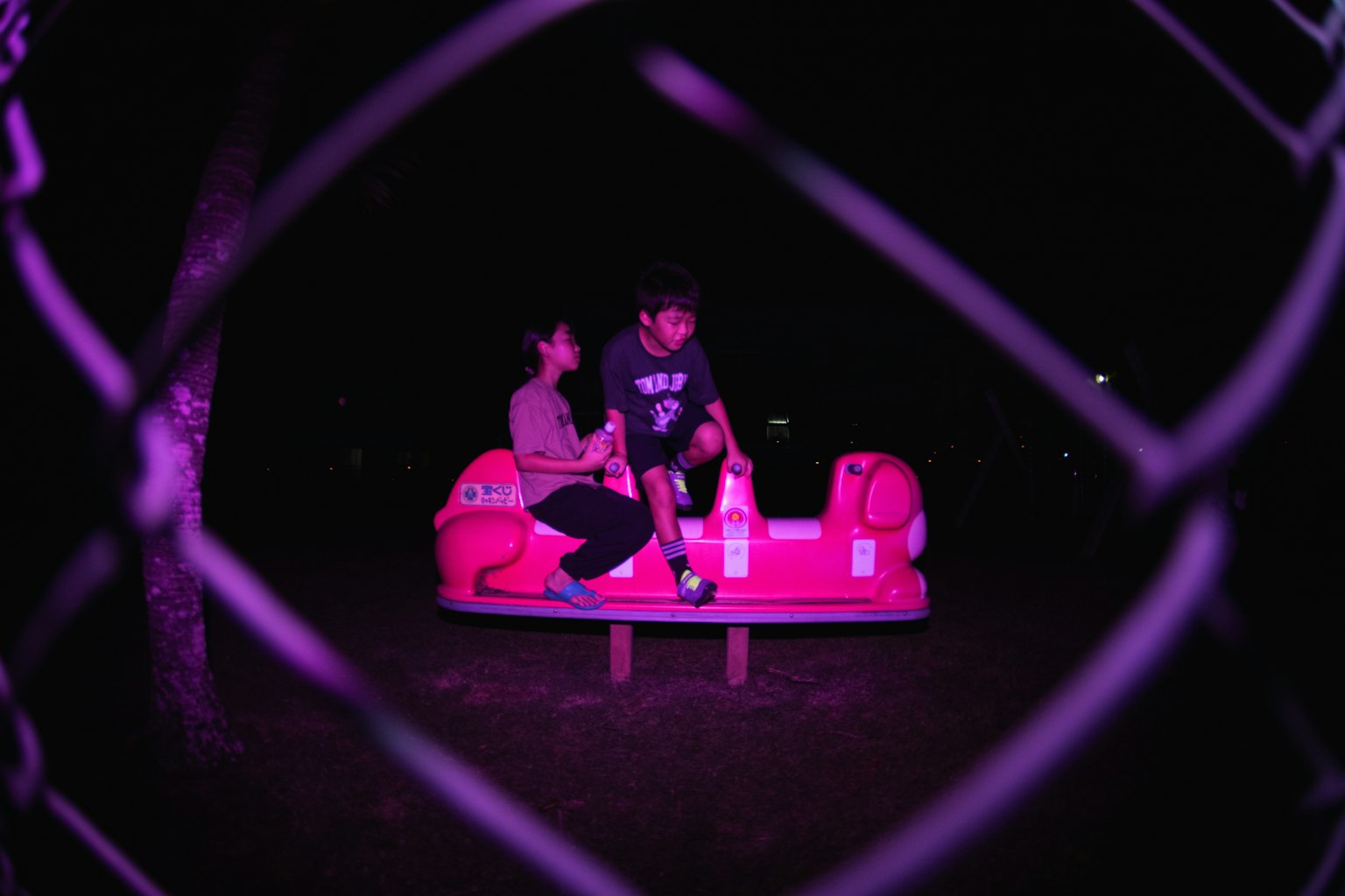 Silhouette d'un homme et d'une femme assis sur un équipement de jeu rose la nuit