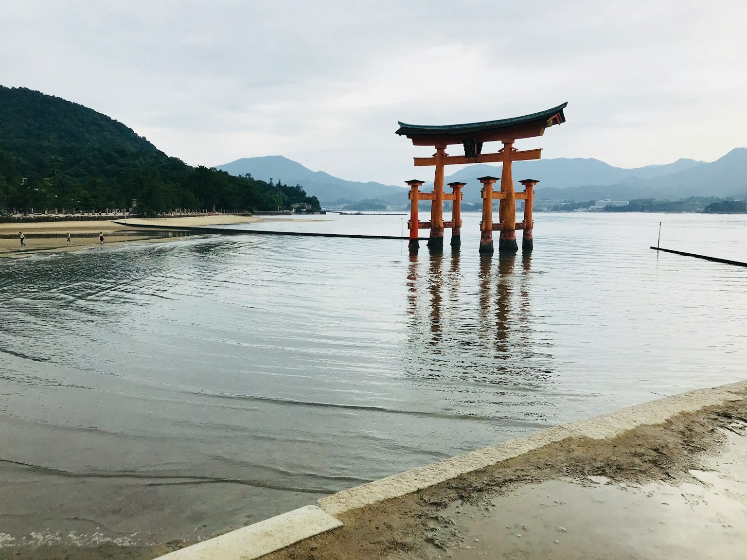 Torii gate standing in calm water with mountains in the background