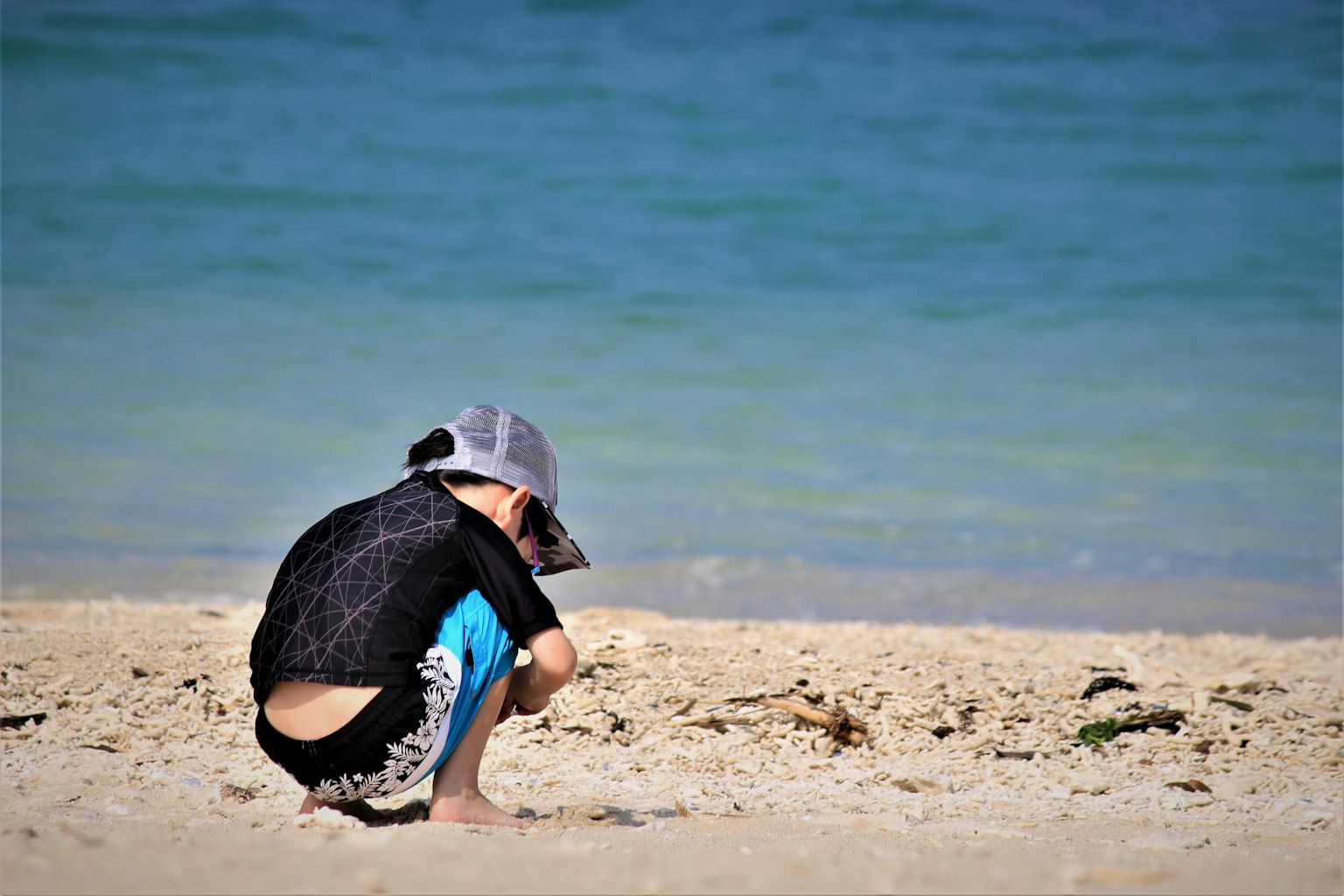 Child playing on the beach wearing a black shirt and blue shorts
