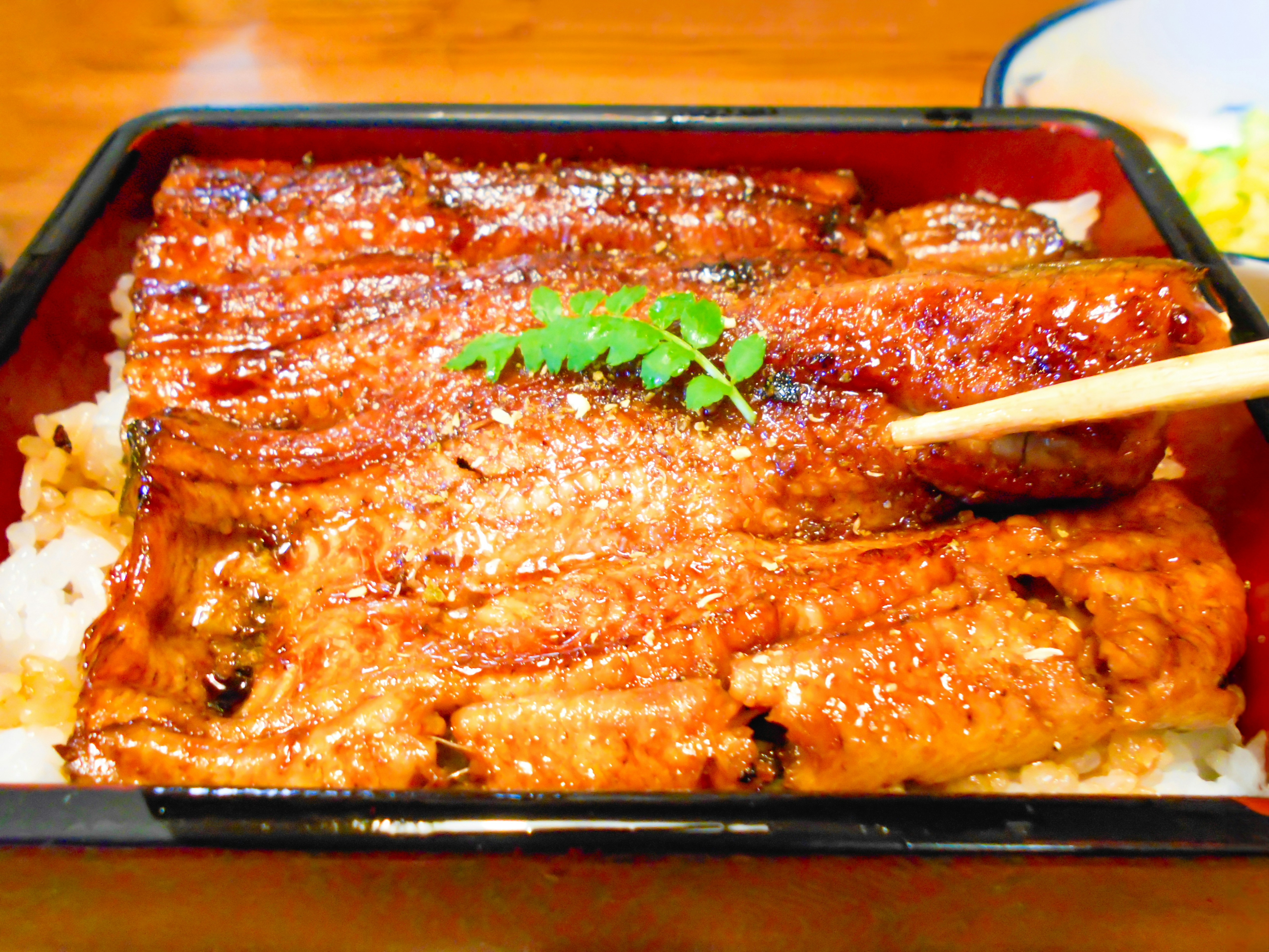 箸でつまんだ焼きうなぎ丼のアップ