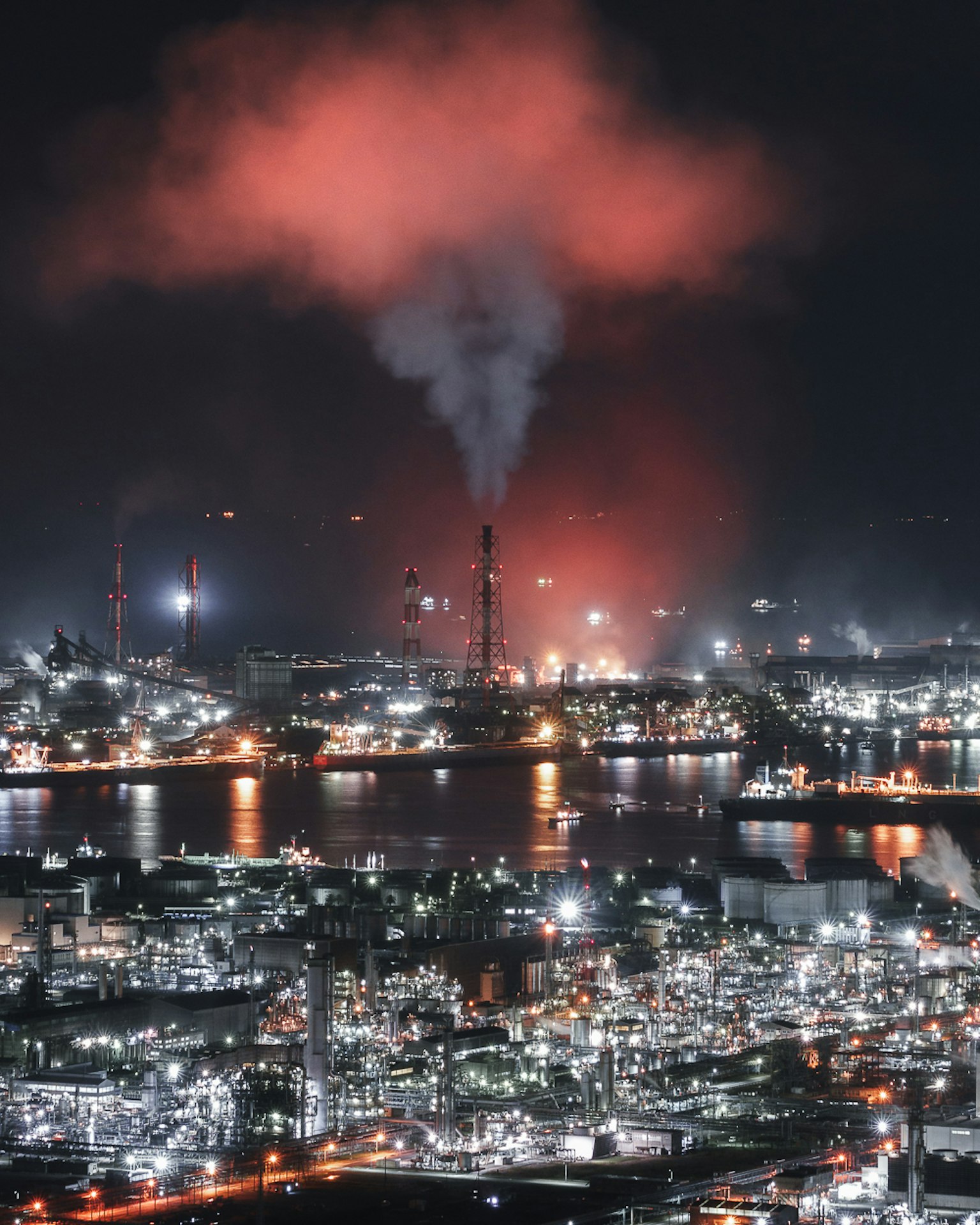 Nighttime industrial landscape with vibrant lights and smoke rising from chimneys