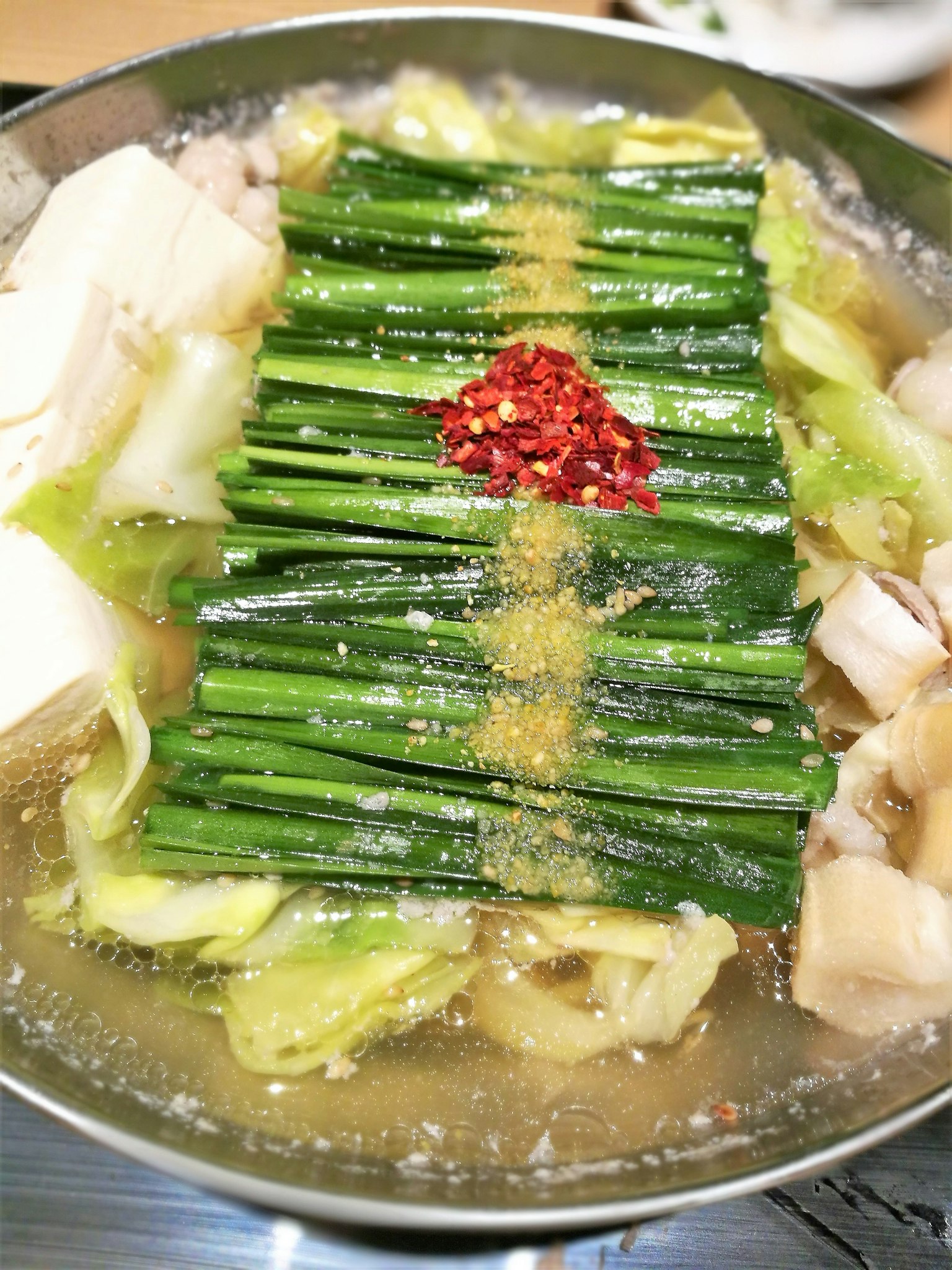 Un piatto di hot pot con pollo, tofu e cavolo, guarnito con cipollotti e peperoncino rosso