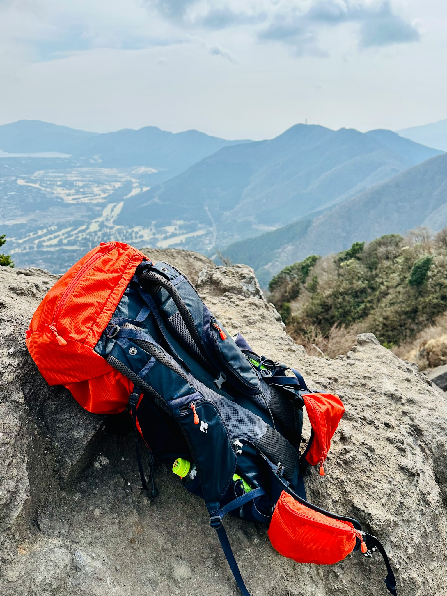An orange backpack resting on a rock with mountains in the background