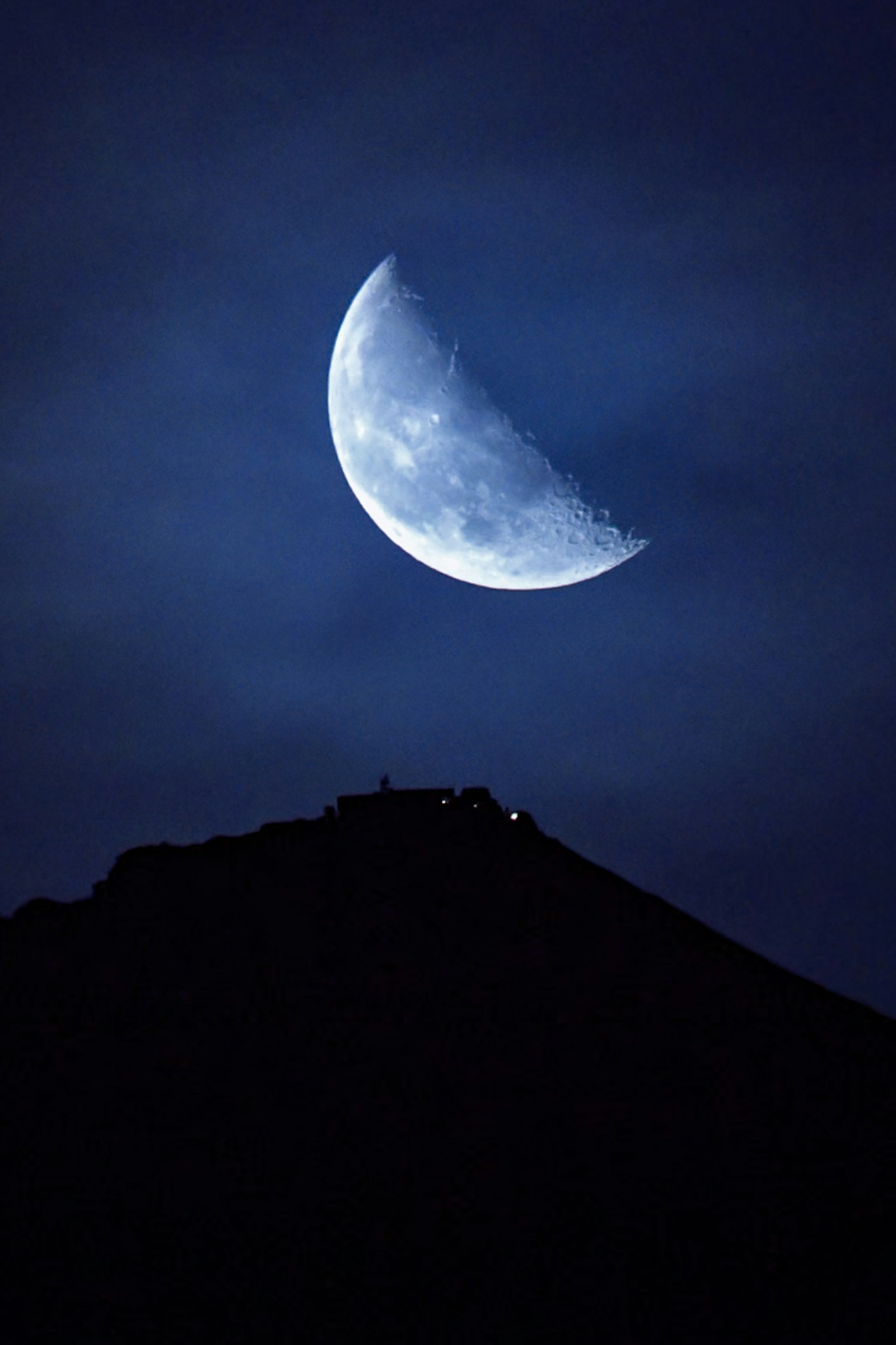 夜空中蓝色的细月亮和山的轮廓