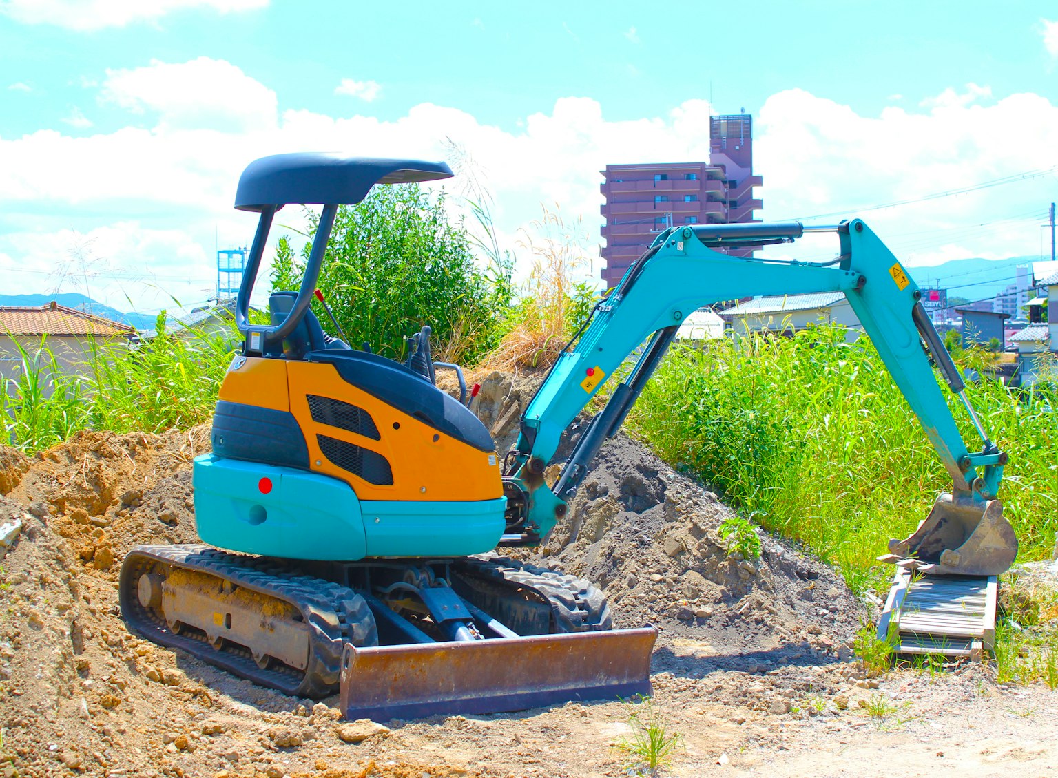 Ein kleiner blauer und orangefarbener Bagger arbeitet auf einem Erdhaufen