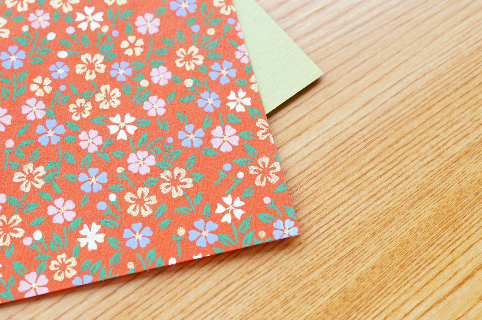 Oranges blumenmusterpapier und grünes papier auf einem Holztisch