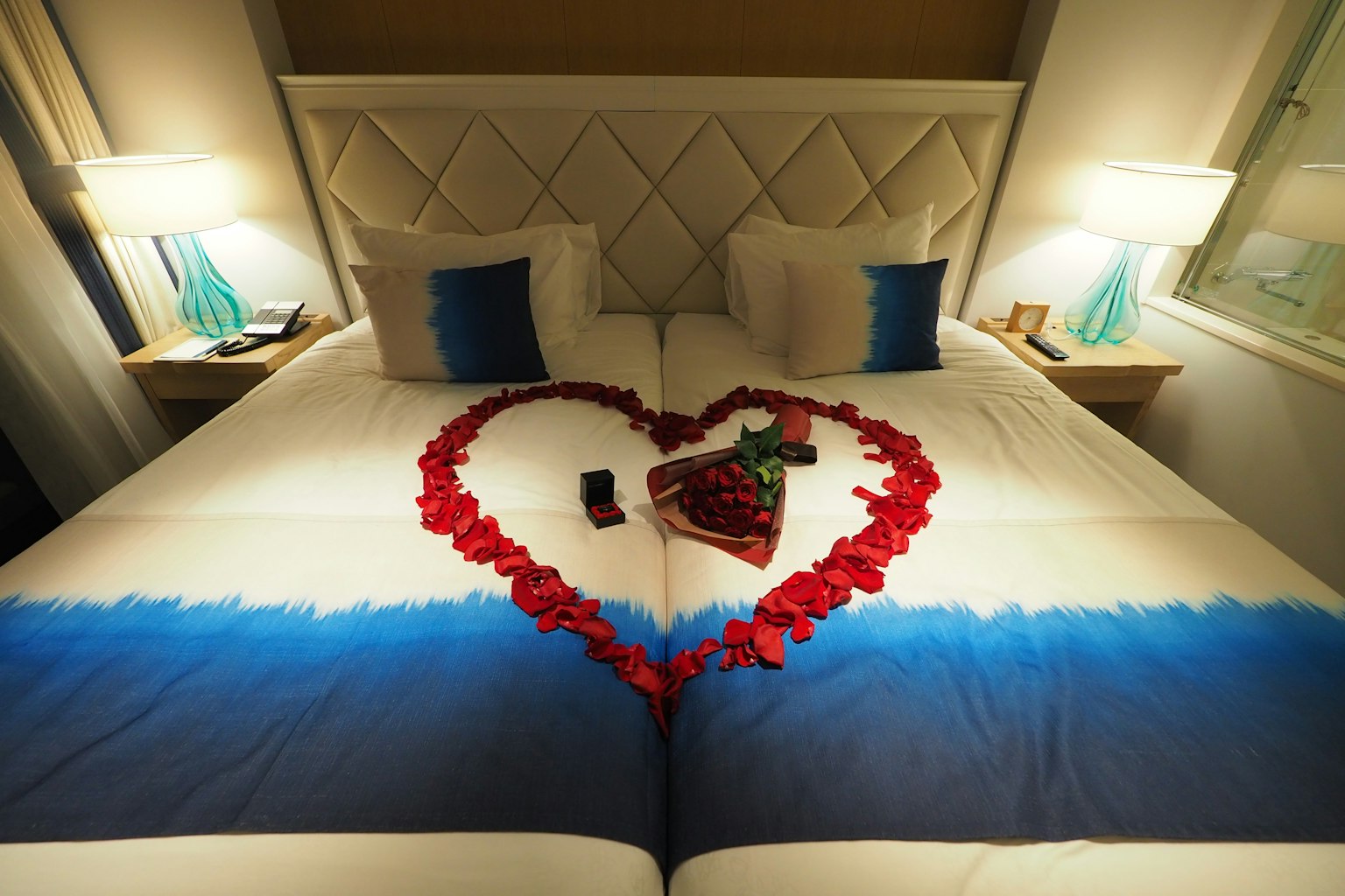 Una cama con sábanas azules y blancas decorada con pétalos de rosa en forma de corazón y pequeños objetos encima