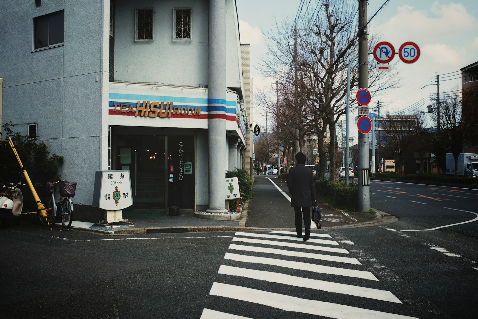 Eine Person, die auf einem Zebrastreifen geht, mit einem Geschäft an der Ecke unter einem blauen Himmel
