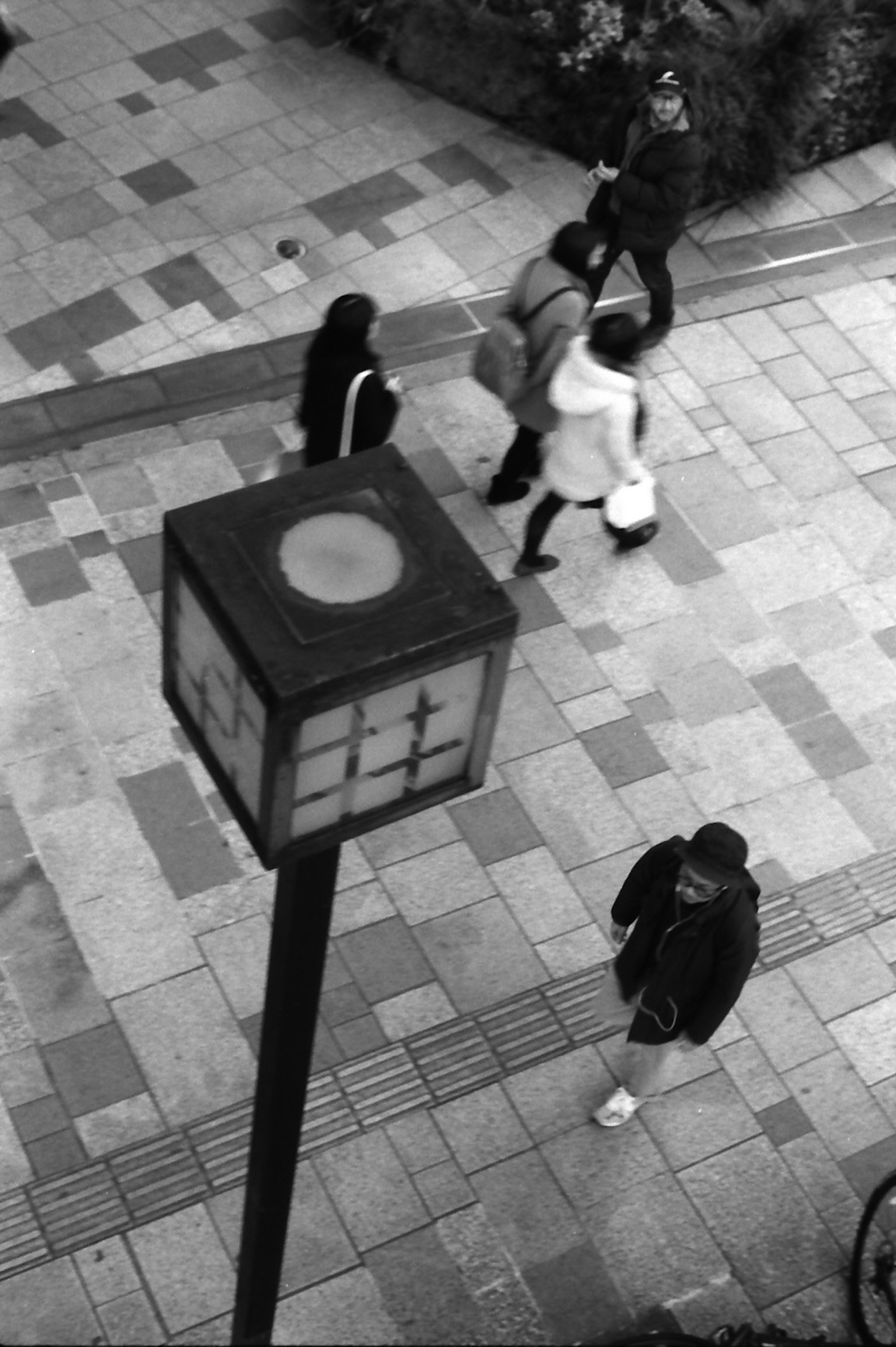 Imagen en blanco y negro que muestra personas caminando y una farola