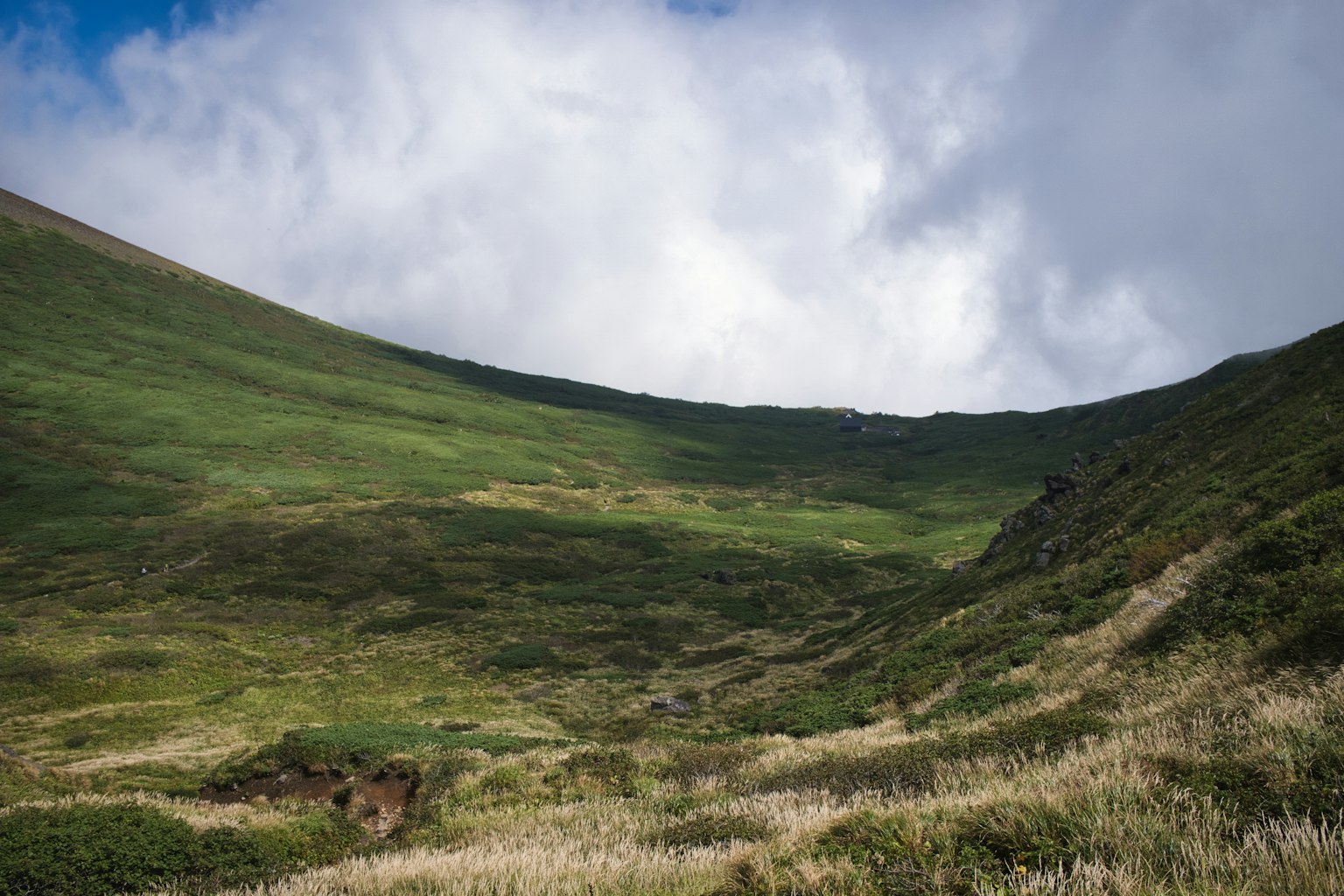 Valle verdeggiante con colline ondulate e cielo nuvoloso
