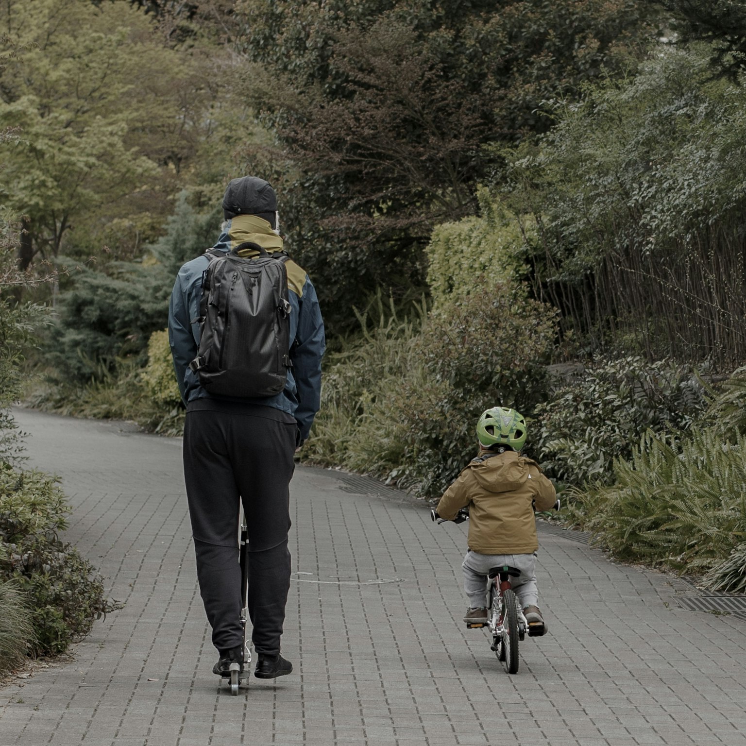 Adulto y niño caminando por un sendero del parque niño montando en bicicleta