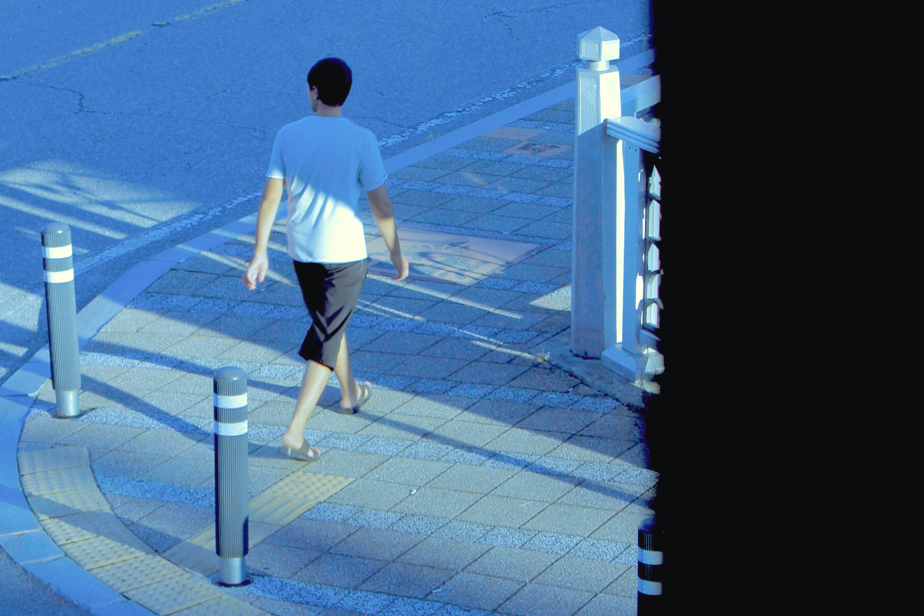 青いトーンの街角を歩く男性の後ろ姿