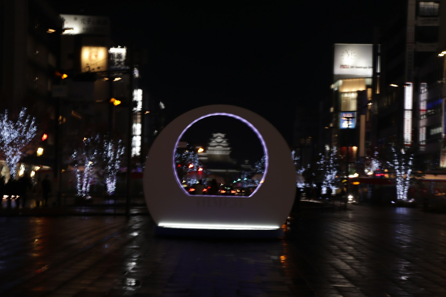 Zirkuläres Denkmal mit beleuchteten Bäumen und Stadtlichtern bei Nacht