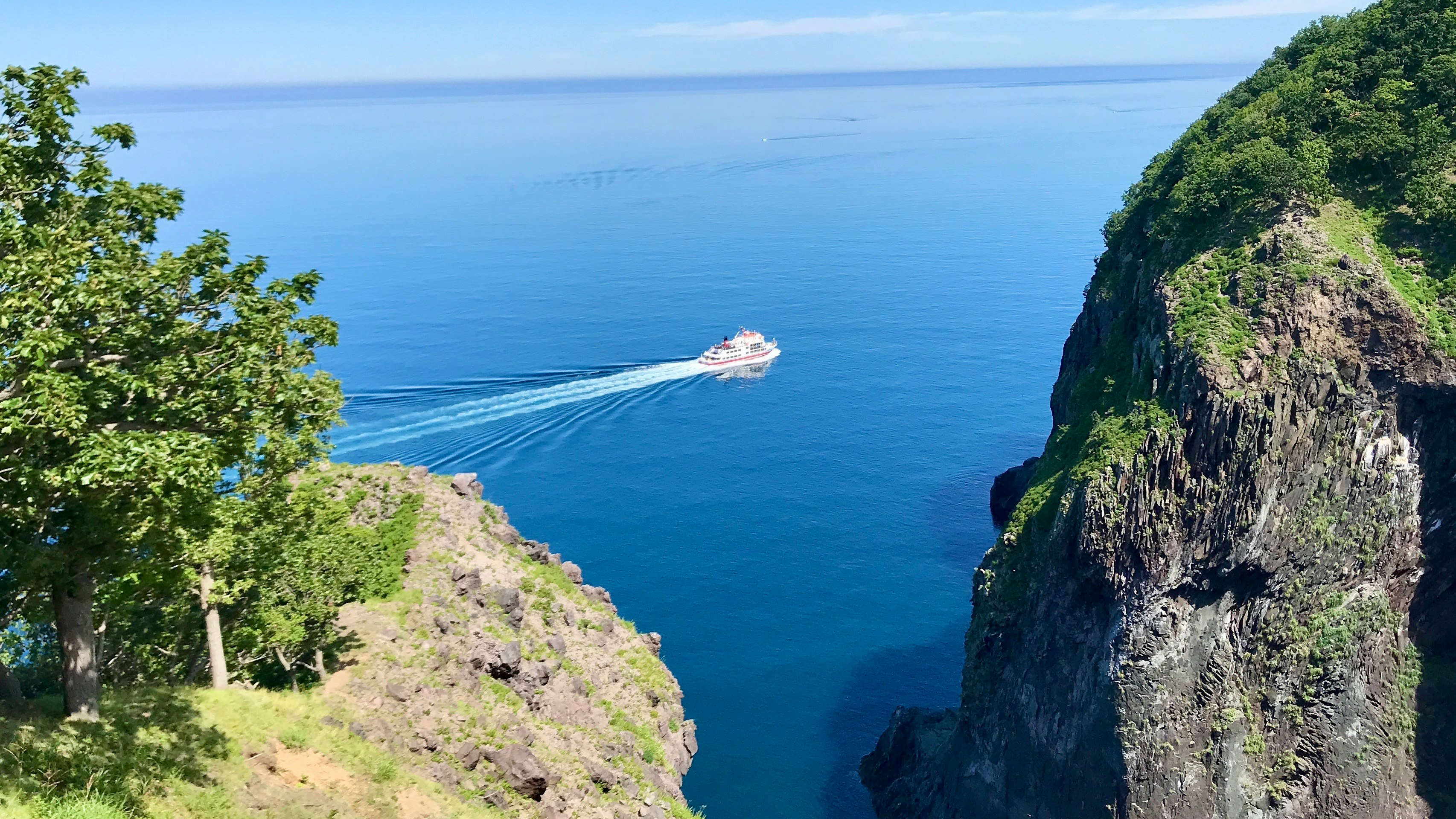 青空の下、知床の断崖と海を行く船
