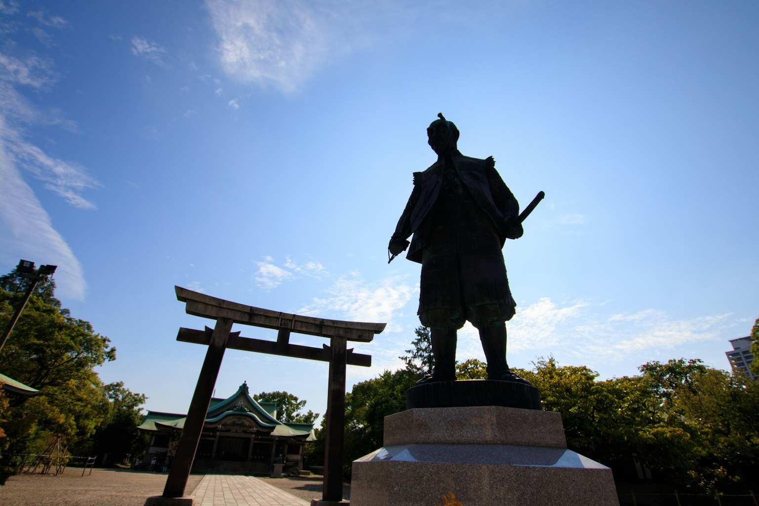 Silhouette d'une statue de samouraï sous un ciel bleu avec un torii