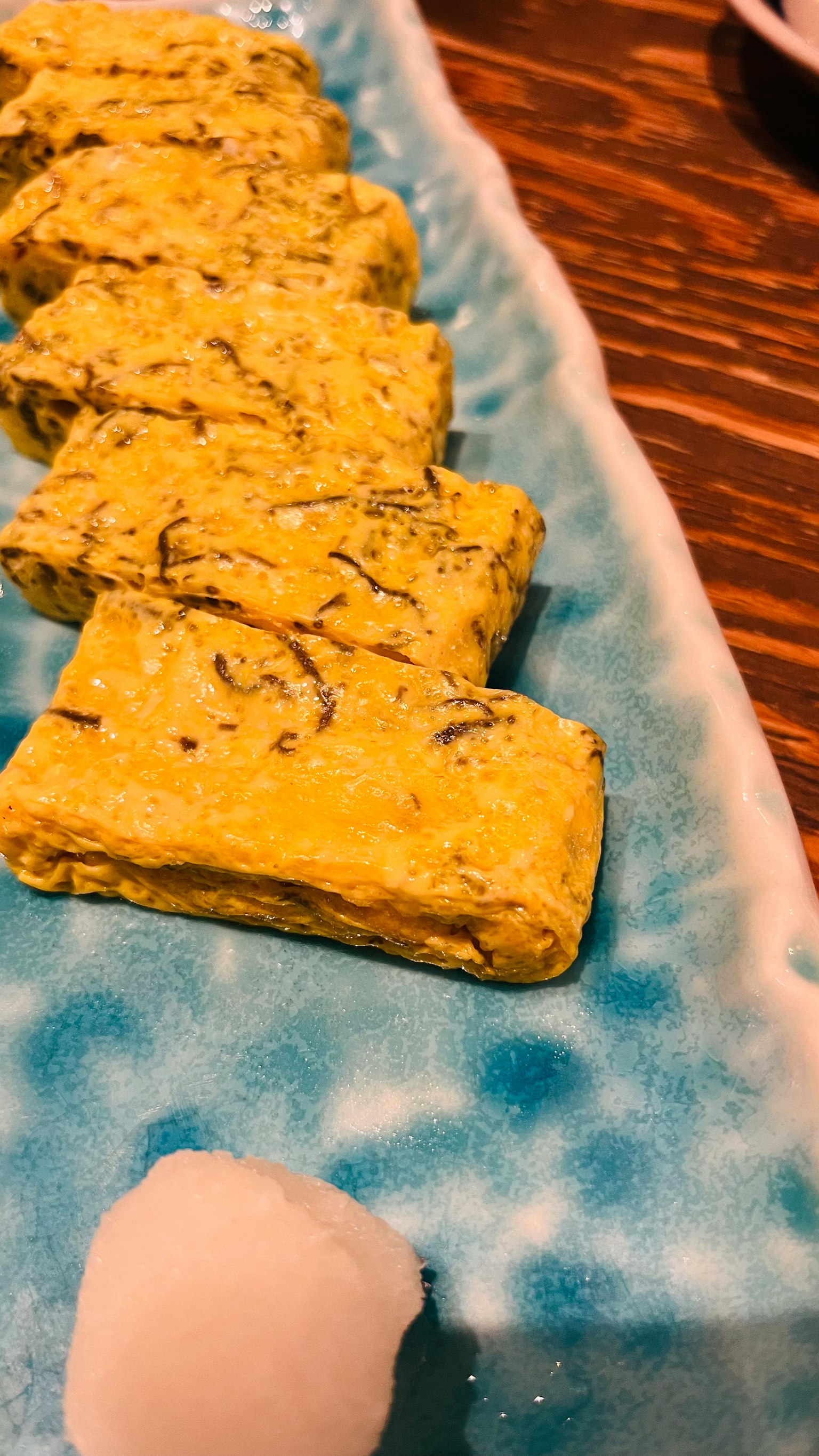 Un bellissimo piatto blu con fette di omelette giapponese e una porzione di daikon grattugiato bianco