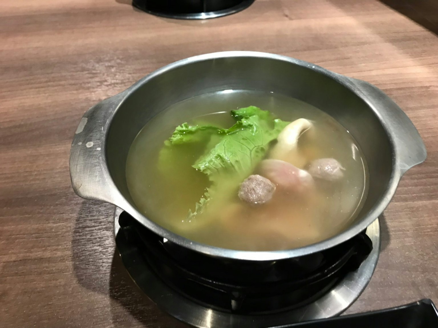Una pentola con brodo, foglie verdi e polpette