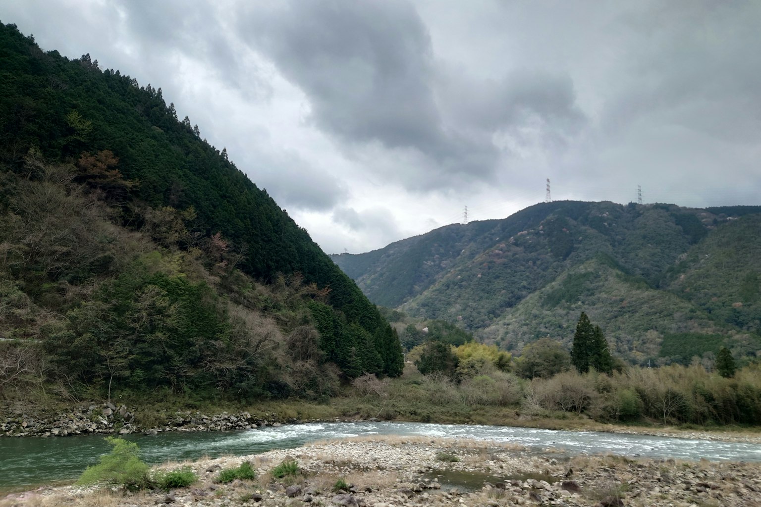 Vista escénica de montañas y río bajo un cielo nublado con un bosque verde exuberante