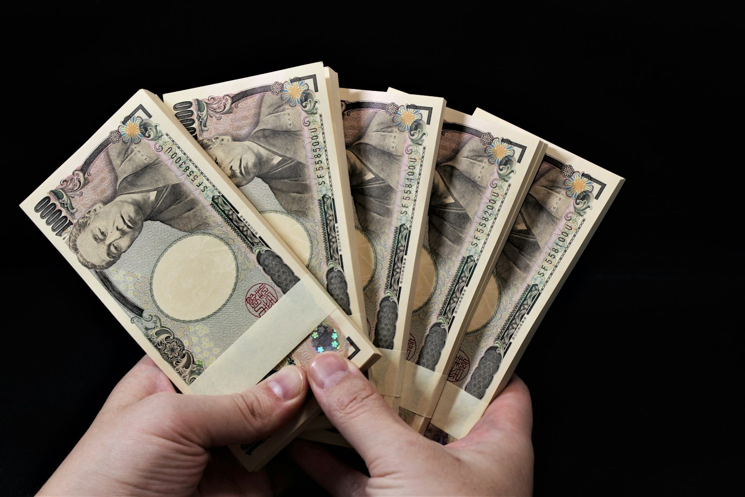 มือที่ถือธนบัตรเยนญี่ปุ่นบนพื้นหลังสีดำ