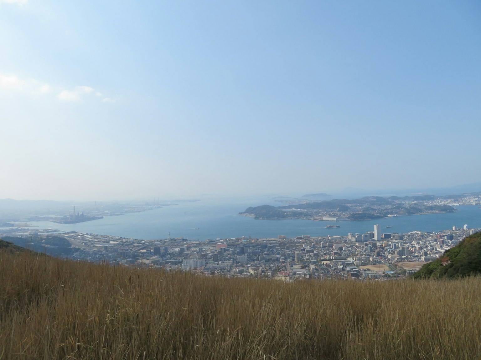 Vista panoramica di un mare blu e di una città con un primo piano d'erba