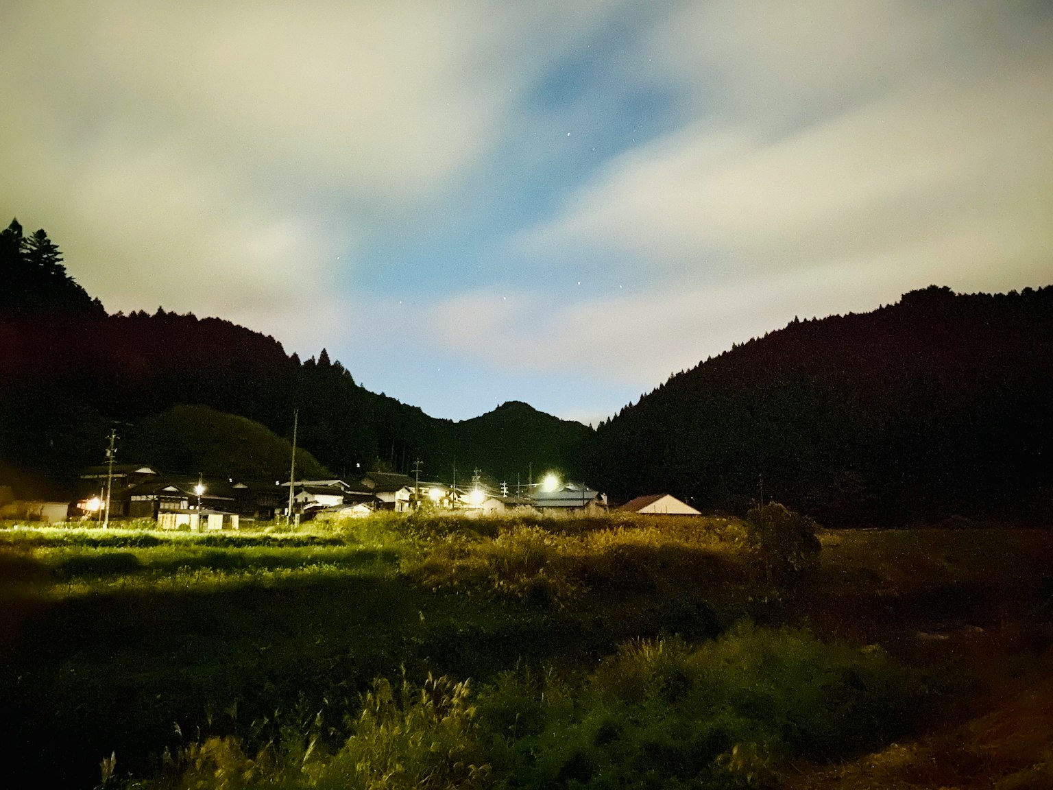 ทิวทัศน์ในยามค่ำคืนของชนบทที่เงียบสงบพร้อมภูเขาและหมู่บ้าน