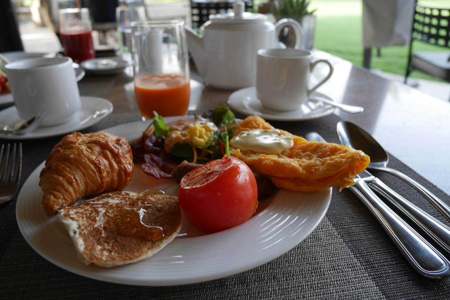 Un plato de desayuno que incluye croissant, tomate, ensalada, plato de huevos y panqueques
