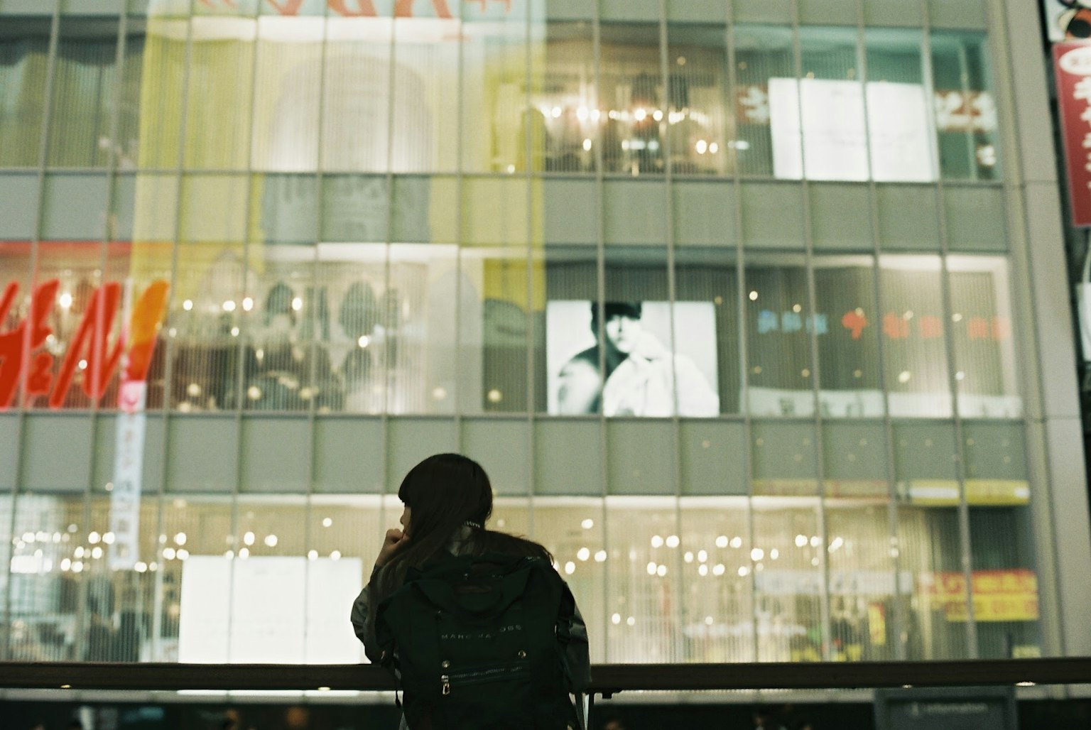 Eine Person steht vor einem Gebäude mit hellen Lichtern, die von den Fenstern reflektiert werden