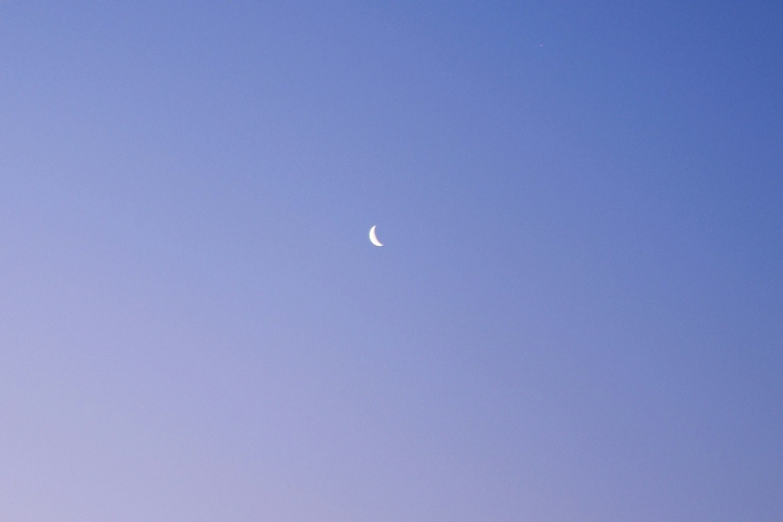 Thin crescent moon against a blue sky