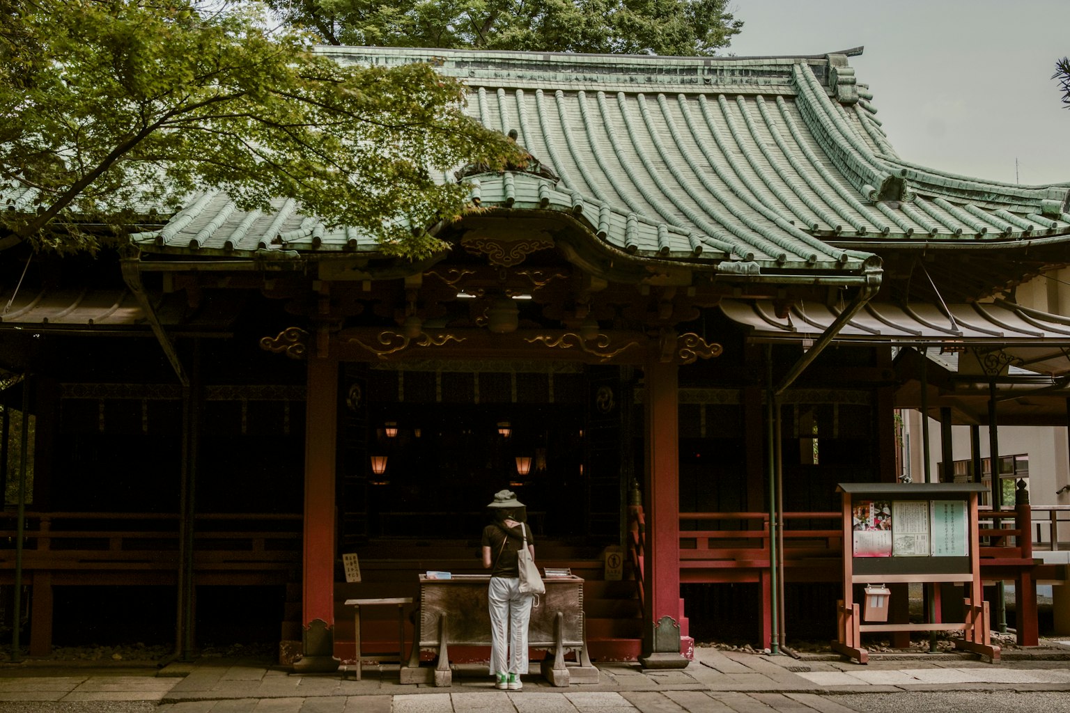 Una mujer de pie frente a un santuario japonés tradicional con un techo verde