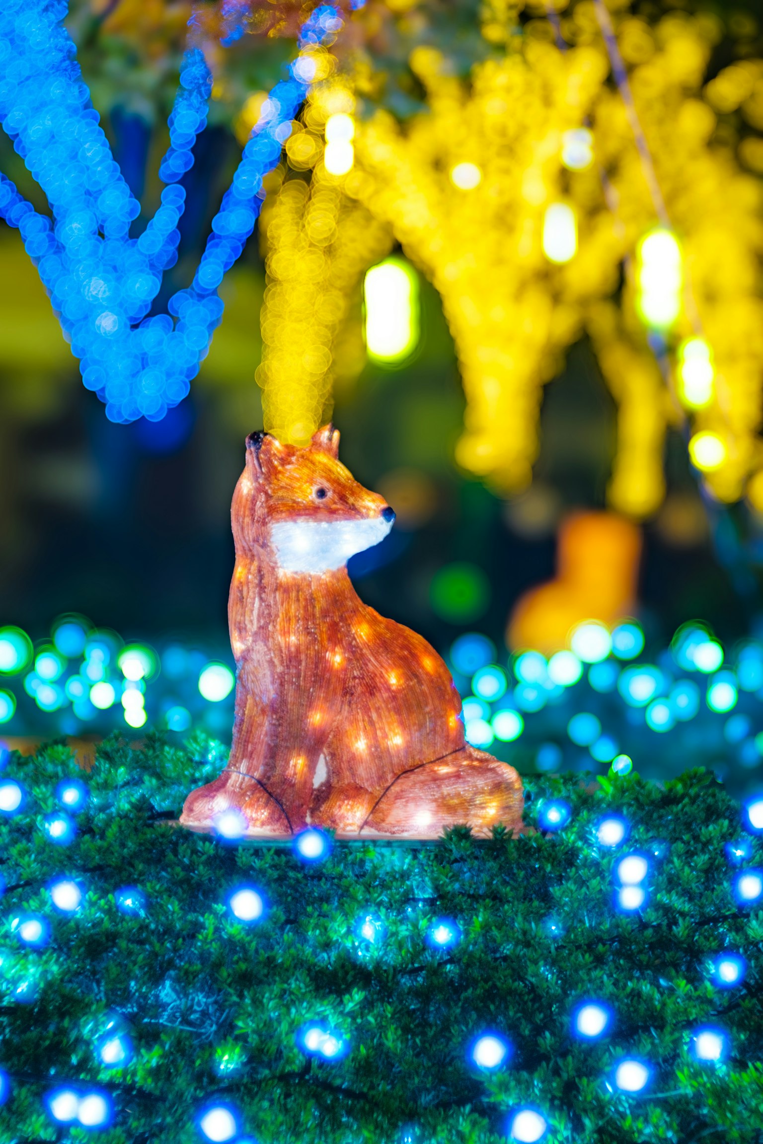 Una estatua decorativa de zorro adornada con luces brillantes se sienta entre luces azules