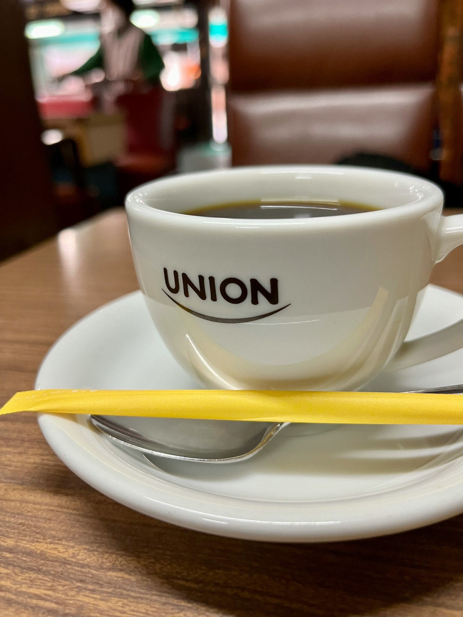 ถ้วยกาแฟสีขาวที่มีโลโก้ UNION และช้อนสีเหลืองบนจาน