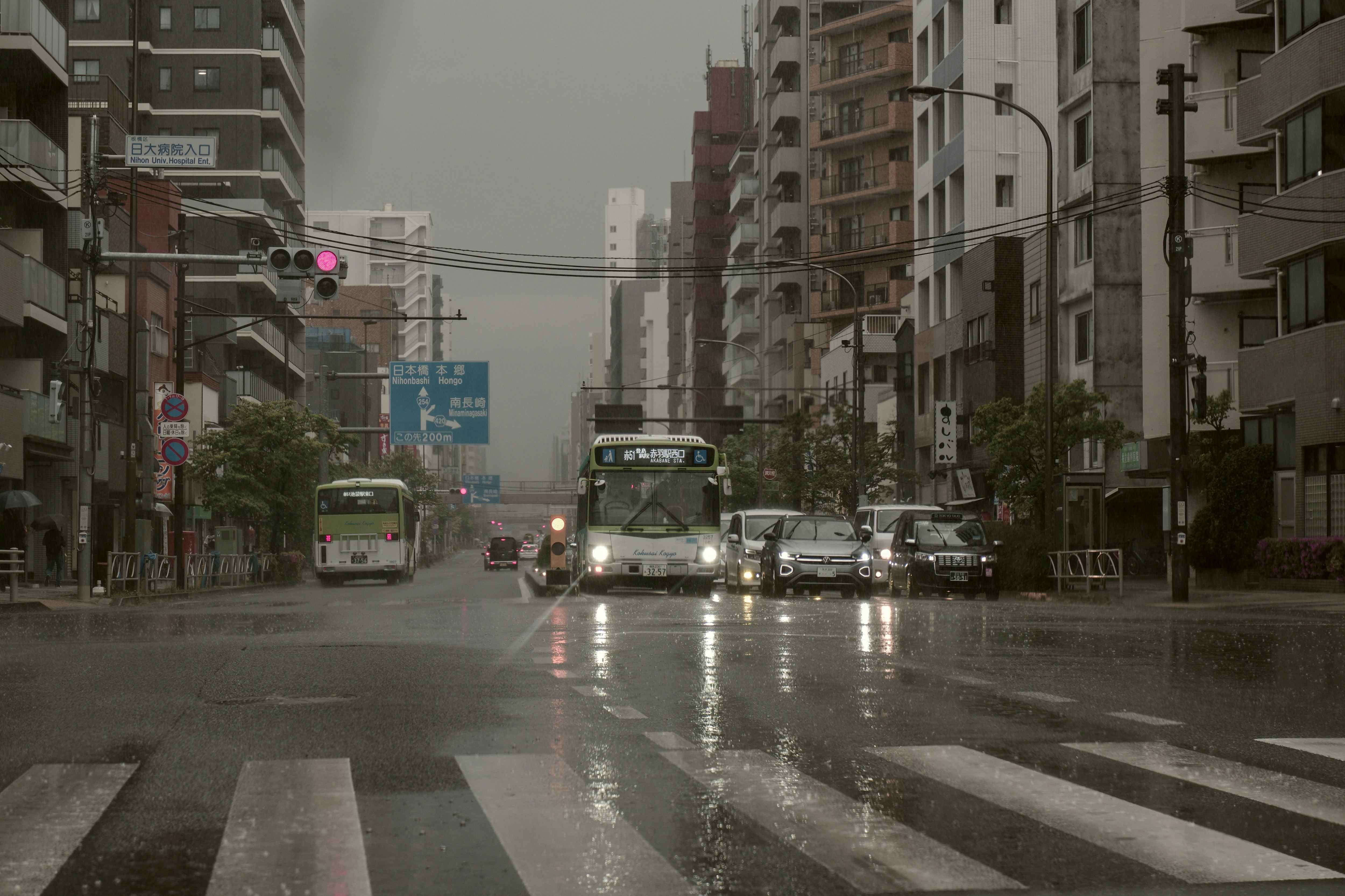 雨の降る都心の交差点を走るバスと車のある街並み