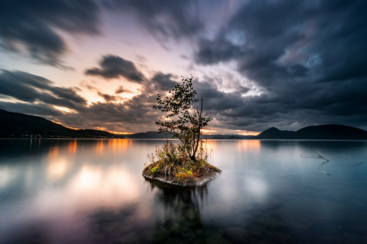 Una scena di lago tranquillo con un'isola piccola e un albero solitario al tramonto