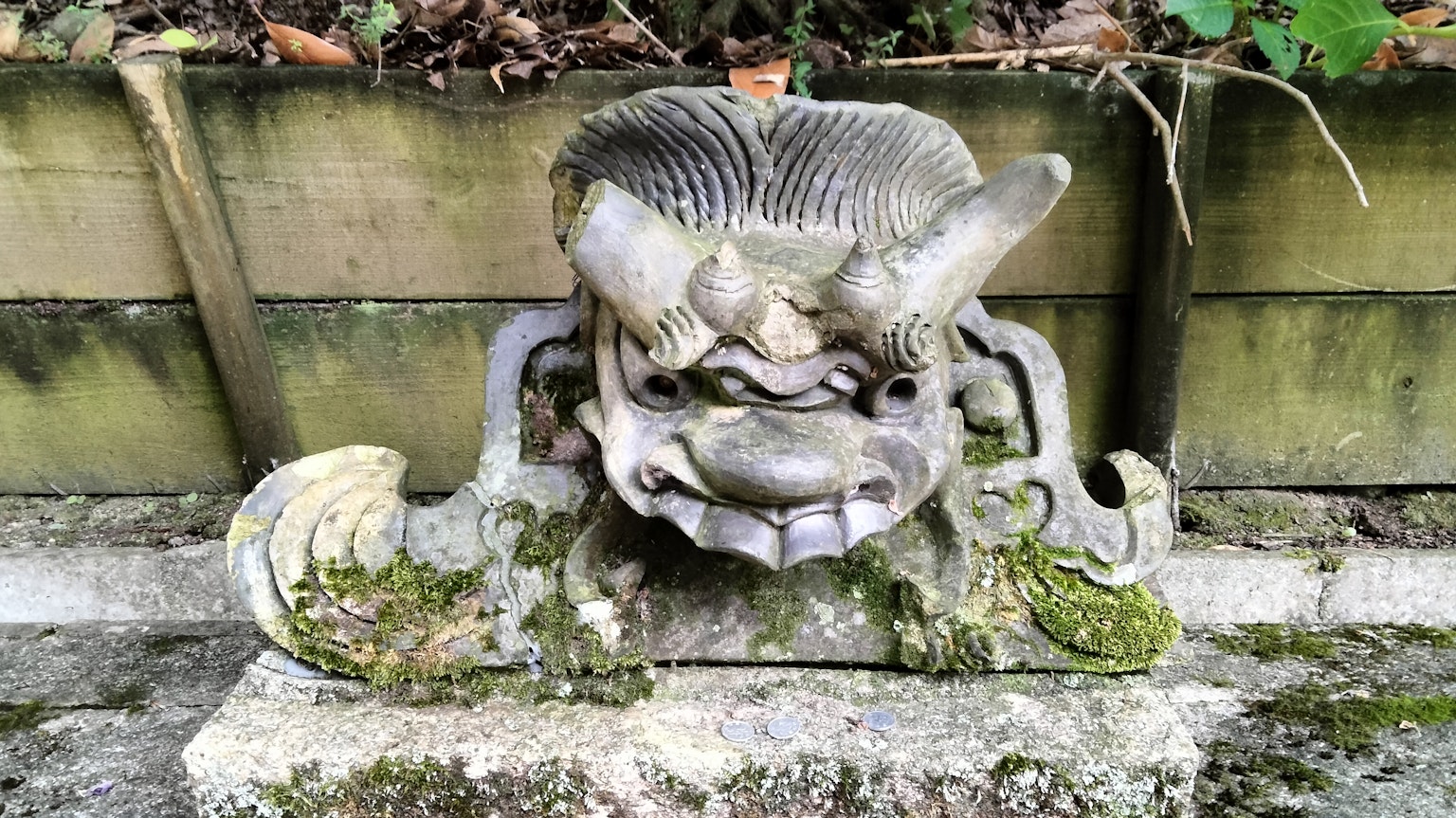 Antica scultura in pietra con un volto simile a un leone e dettagli coperti di muschio