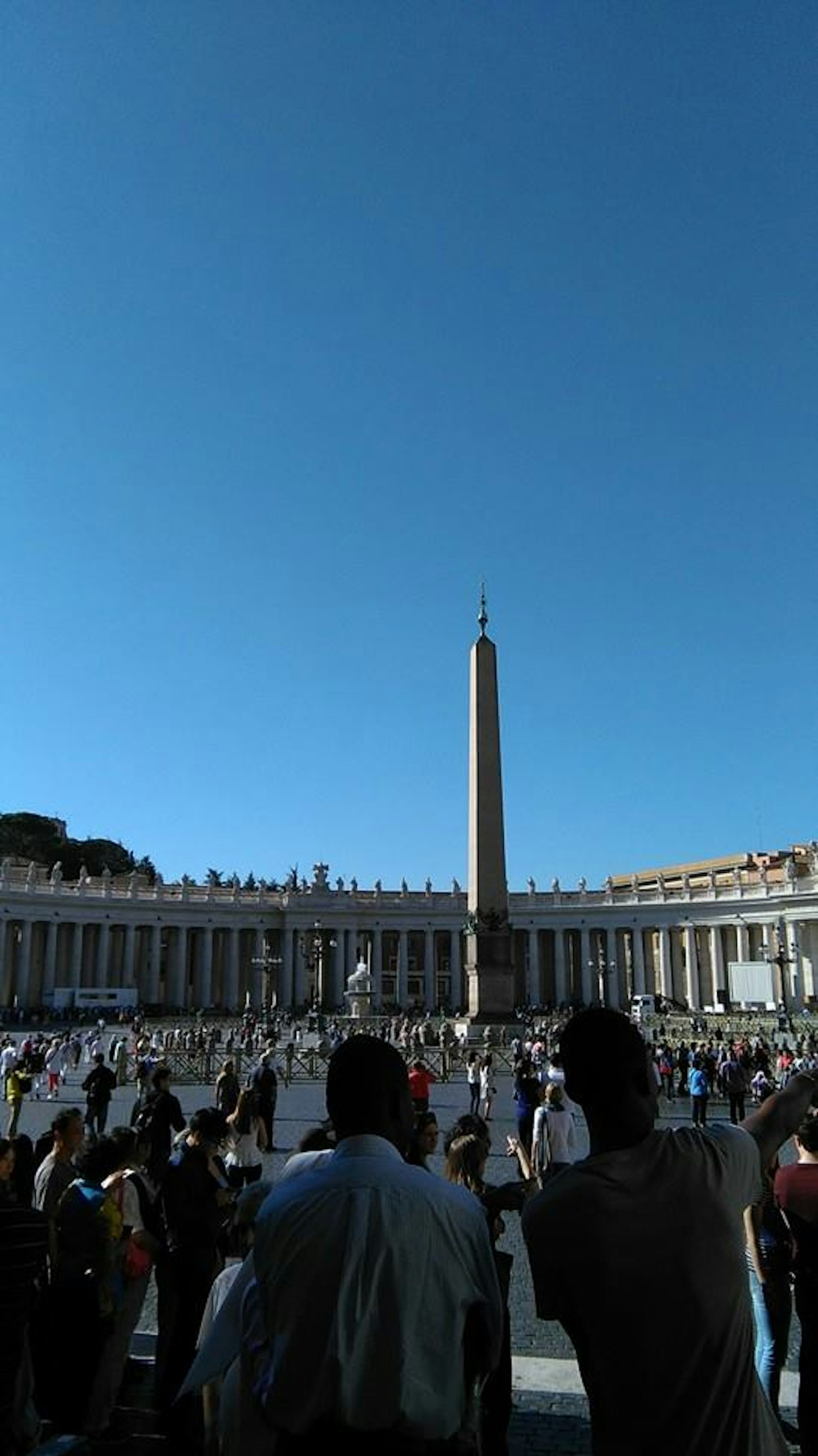 Vista de la Plaza de San Pedro en el Vaticano con personas y un obelisco bajo un cielo azul