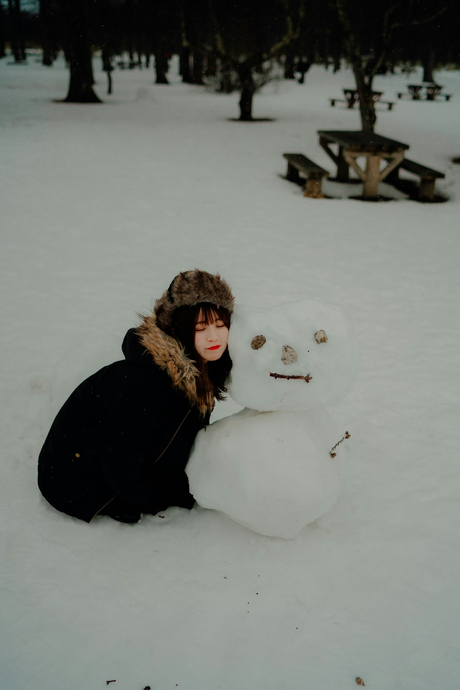 Mujer sentada en la nieve con un muñeco de nieve