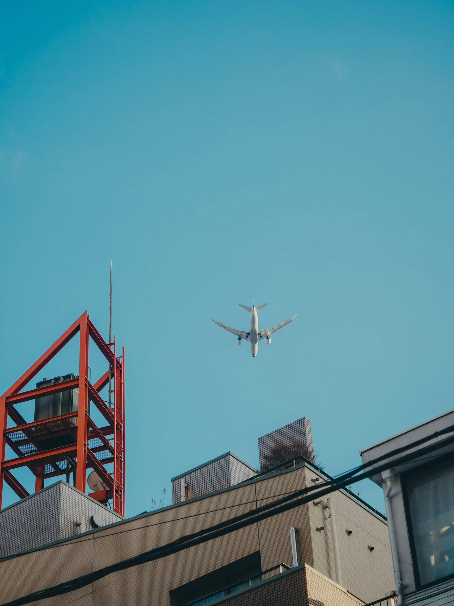 Airplane flying in a blue sky above city buildings with a red tower